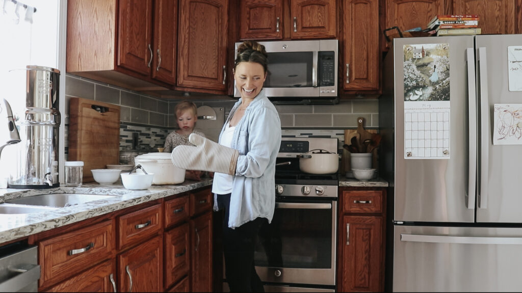 Christian homemaker prepares food and is wearing an oven mit. She is smiling at someone off camera.